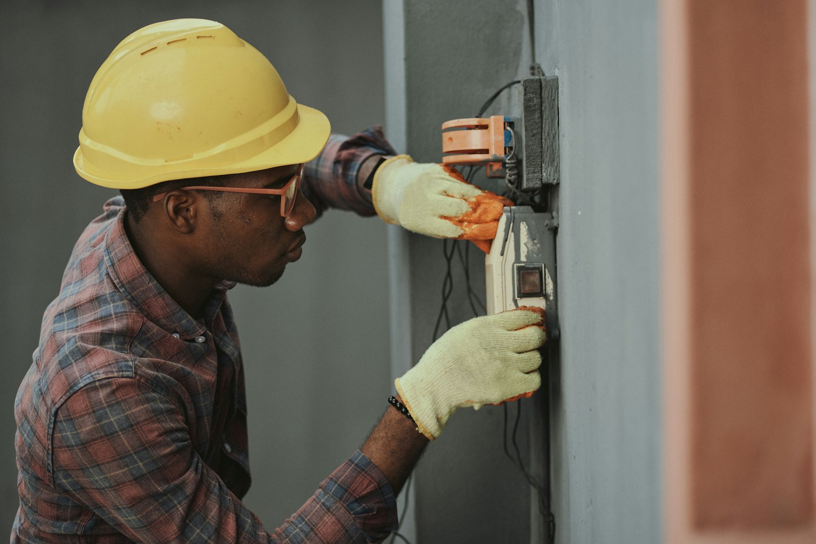 An electrician in a hard hat wiring a panel
